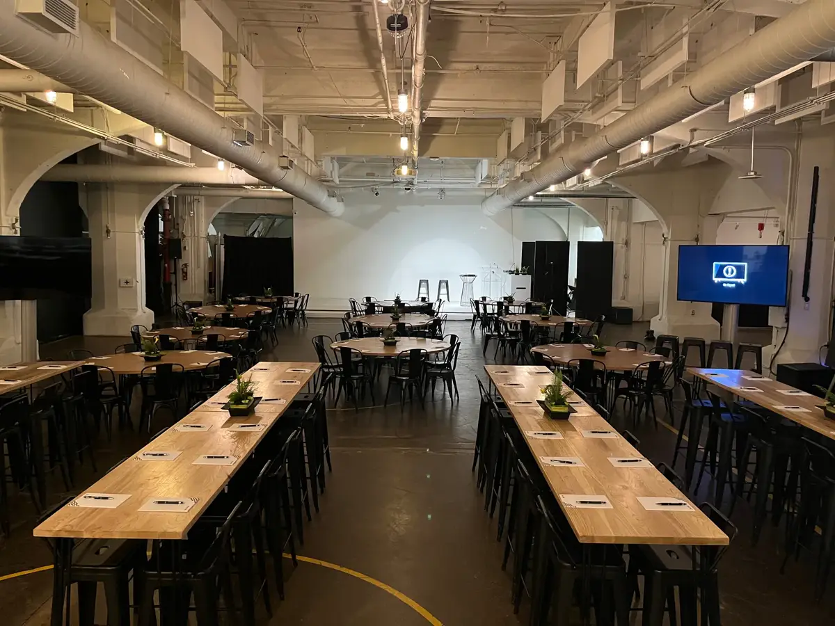Salle d'évènement corporatif aménagée avec longues tables et tables rondes devant une scène et un écran